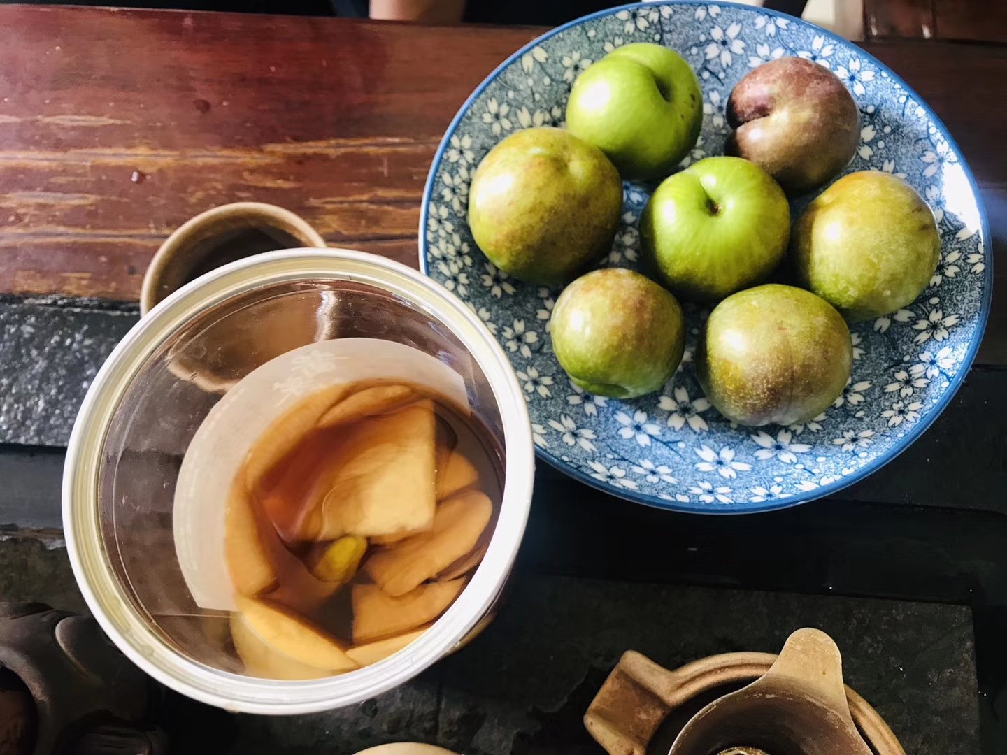 一张餐桌上的创意料理展示:左侧是一碗切片的新鲜三华李子搭配希腊酸奶和坚果碎,右侧是一杯用三华李子调制的冰镇气泡饮品,玻璃杯外凝结水珠,旁边摆放一把木勺和柠檬片装饰 三华李子美食创意搭配