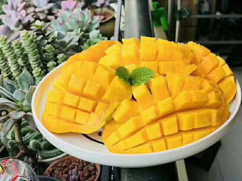 一个被横向切开的海南金煌芒,露出厚实金黄的果肉,果核纤薄如纸片,果肉表面有晶莹的果汁反光,旁边搭配一片绿叶和半个柠檬片,背景为浅色木纹桌面,整体画面清新自然,突出水果的新鲜与高品质 切开的海南金煌芒特写图