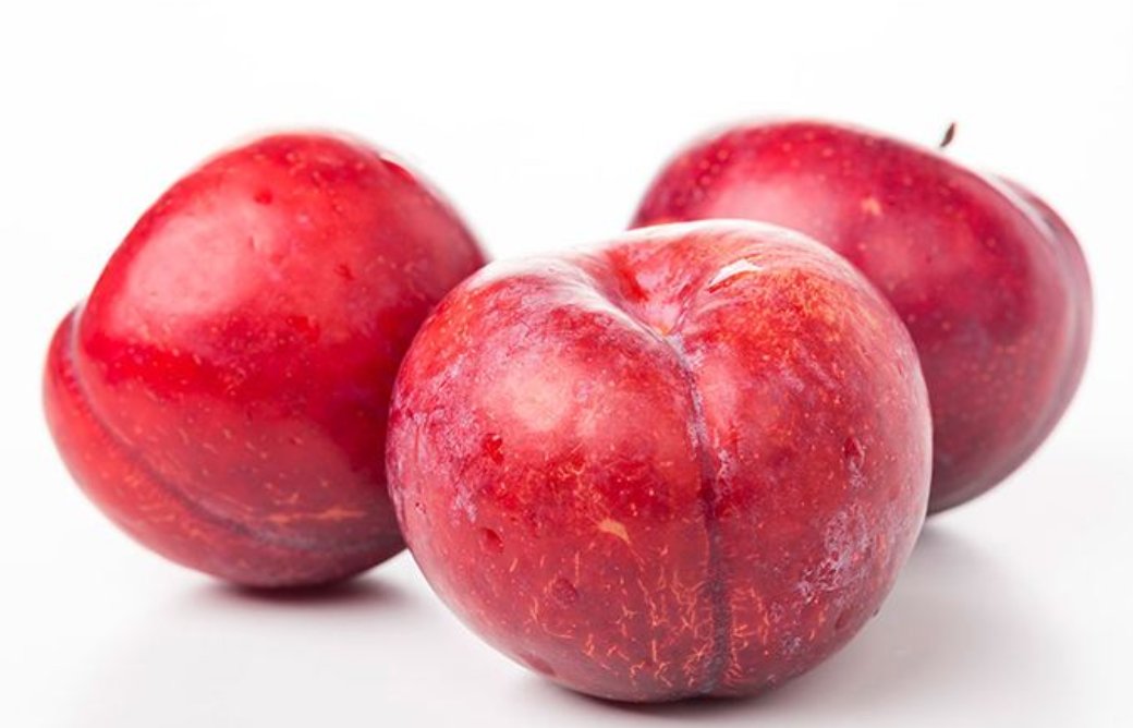 一颗成熟饱满的红布林,表皮呈现深红至紫红色光泽,表面带有天然果粉,切开后果肉呈金黄色,汁水丰富,背景为自然果园环境 红布林特写