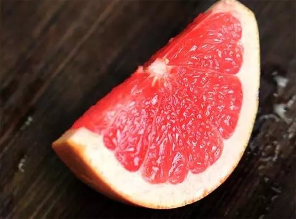 一颗成熟饱满的红马斯卡丁葡萄柚,果皮呈浅粉红色至淡橙色,表面光滑略带光泽,切开后果肉呈鲜艳的玫瑰红至深粉红色,汁胞饱满,无明显籽粒,背景为阳光照射下的果园环境 红马斯卡丁葡萄柚特写