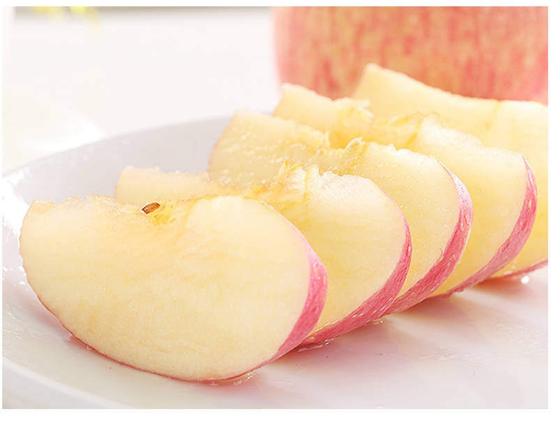 一颗被横向切开的嘎啦苹果,露出白色的果核和放射状排列的种子,果肉呈淡黄色,汁水丰富,切面晶莹剔透,旁边配有小勺和白色瓷盘,突出其新鲜多汁的特点 切开的嘎啦果特写展示果肉结构