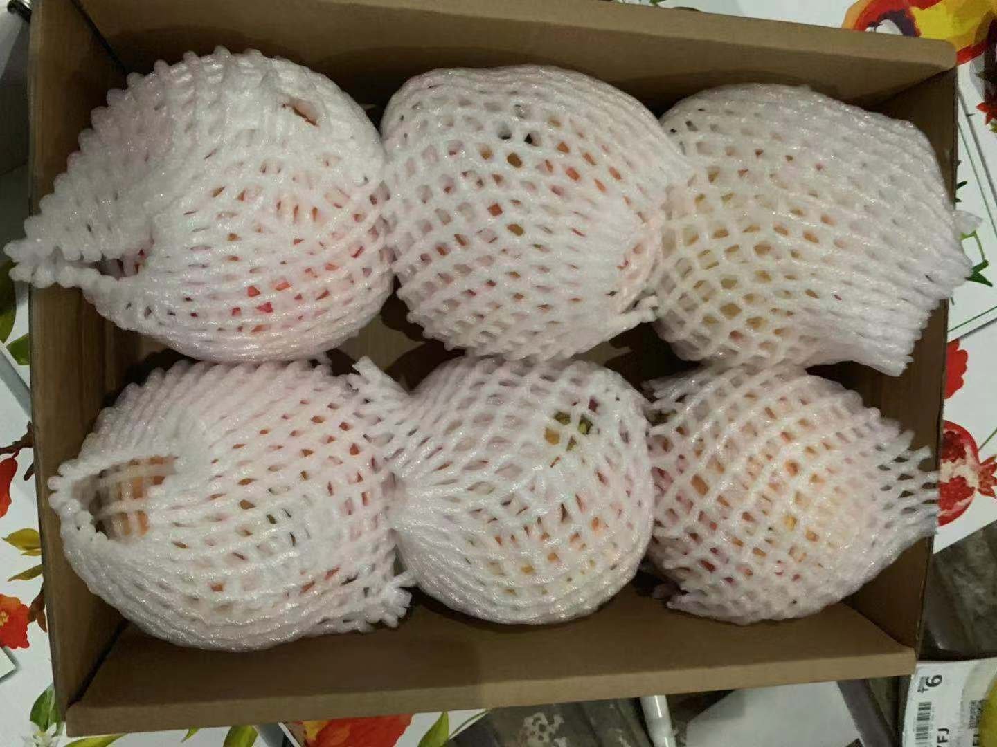 一盒精美的软籽石榴礼盒,内含6颗大小均匀、表皮呈深红至紫红色的软籽石榴,果实表面光滑有光泽,背景为木质餐桌与绿植,营造出自然健康的氛围 软籽石榴礼盒装展示