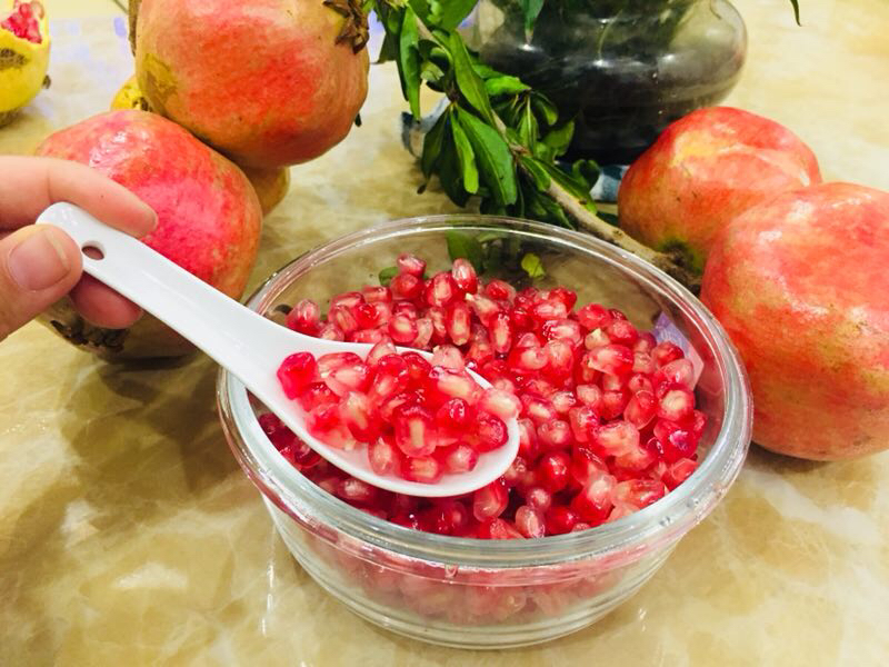 生活化实拍:展示正确食用方式——用门齿轻咬软籽石榴籽,可见薄种皮未破裂、紫红胚乳汁液渗出,强调'嚼而不吞皮、食其仁'的动作细节;计量勺旁标注标准日摄入量参考 家庭厨房场景:白瓷盘中盛放去皮软籽石榴果肉,特写镜头聚焦于用牙齿轻咬一颗籽粒,汁液微溢、种皮完好包裹紫红胚乳,旁边放置计量勺标注'5g=约15粒'