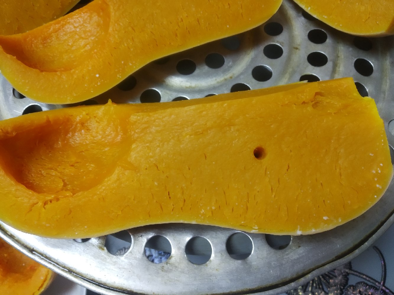 一碗热气腾腾的奶油南瓜圆的盛放在白色瓷碗中，周围点缀着几片桂花花瓣，背景是木质餐桌与秋日落叶装饰