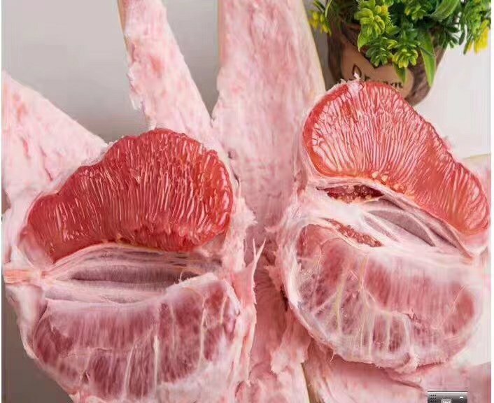 一个完整的琯溪红肉蜜柚被横向切开,露出鲜艳的粉红色果肉,汁胞饱满分明,果瓣排列整齐,表面有晶莹水珠,背景为木质餐桌,体现自然健康的饮食场景 琯溪蜜柚切开特写图