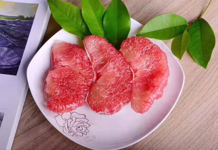 近距离拍摄三红柚鲜红多汁的果肉细节,晶莹剔透的汁胞清晰可见;右侧是一碗混合水果沙拉,包含三红柚瓣、蓝莓、香蕉片和薄荷叶,旁边放着一把小叉子,展示日常健康饮食搭配 三红柚果肉特写与食用场景