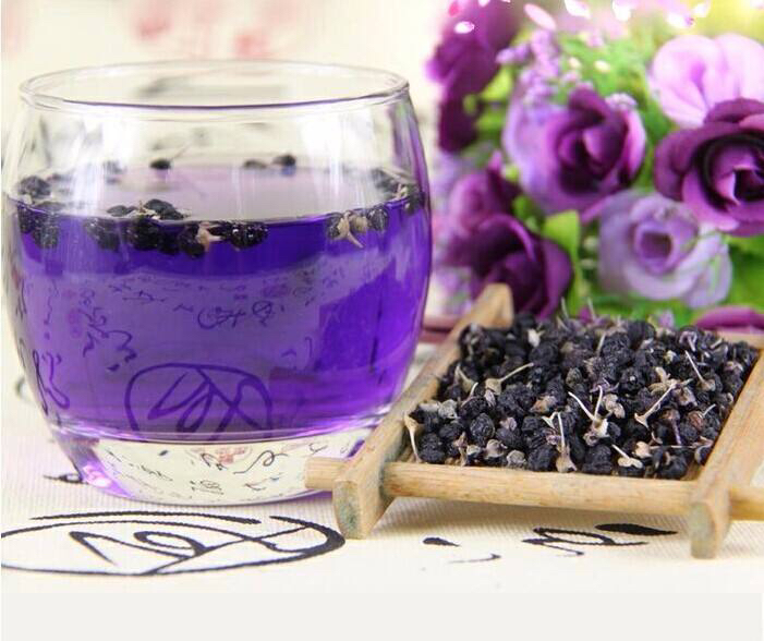 高清俯拍图:左侧为散装金丝皇菊干花,花瓣呈放射状金黄色丝线,完整未碎;右侧为野生晒制黑枸杞干果,颗粒饱满呈深紫黑色,表面有自然白霜;背景为浅色麻布纹理,旁边配有玻璃杯中正在冲泡的茶汤,呈现淡紫色渐变色泽 金丝皇菊与黑枸杞干品对比图