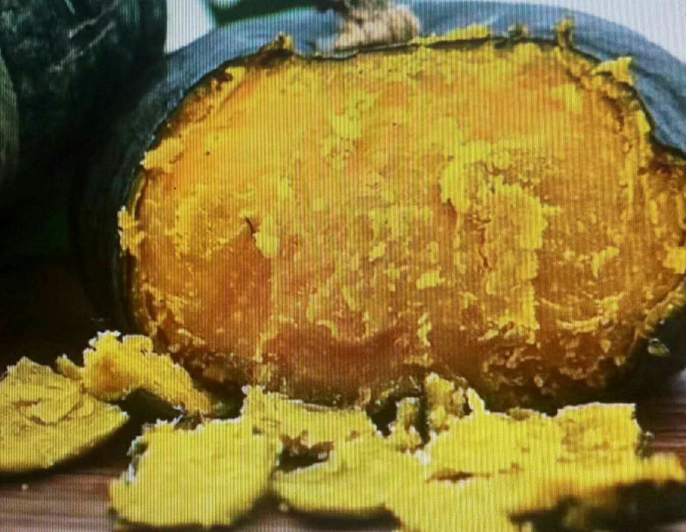 一个被横向切开的金丝板栗南瓜,露出内部金黄色的瓜肉,纹理呈放射状丝线结构,中心为少量扁平瓜籽;背景为白色陶瓷盘,光线柔和,突出瓜肉色泽与质地细节 切开的金丝板栗南瓜横截面特写