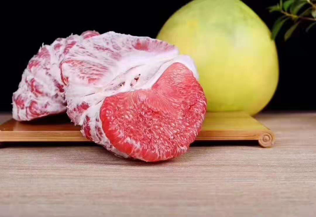 一个切开的琯溪蜜柚特写,果肉呈粉红色(红心蜜柚),汁水饱满,果粒分明,旁边摆放着完整的青黄色蜜柚果实,背景为木质餐桌,体现自然健康的生活方式 单个琯溪蜜柚特写