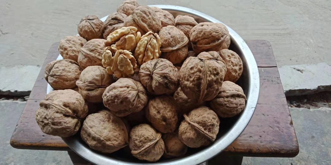 一位女性厨师正在厨房案板上用手轻轻掰开一颗薄皮核桃,旁边摆放着一碗刚取出的完整核桃仁,背景中有燕麦、蓝莓和希腊酸奶组成的早餐碗 一位女性厨师正在厨房案板上用手轻轻掰开一颗薄皮核桃,旁边摆放着一碗刚取出的完整核桃仁,背景中有燕麦、蓝莓和希腊酸奶组成的早餐碗