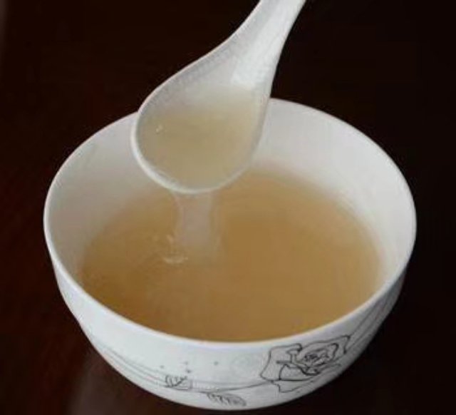 玻璃碗中盛放的白色浓稠淮山粉葛椰奶羹，表面撒有干桂花，旁边搭配木质汤匙