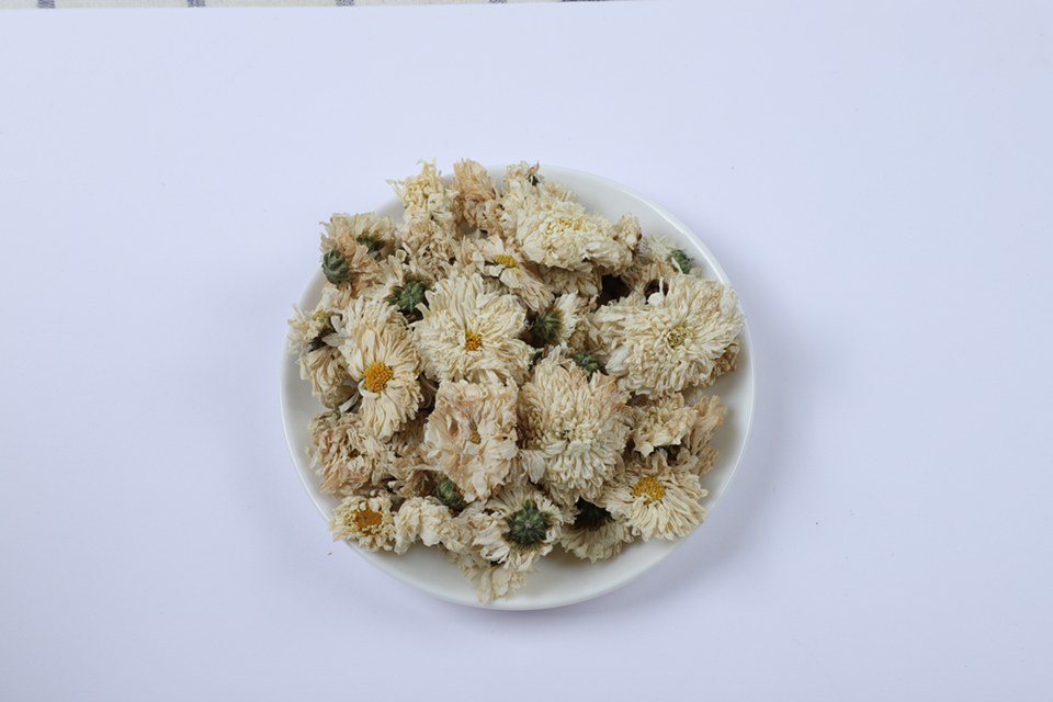 左侧为胎菊王干品,呈紧实金黄色花苞状,表面覆盖细密绒毛;右侧为贡菊干品,花朵已部分开放,花瓣舒展,颜色洁白,中心花蕊明显可见。背景为木质茶盘,配有玻璃公道杯与白瓷品茗杯,体现传统冲泡场景 胎菊与贡菊干品对比图