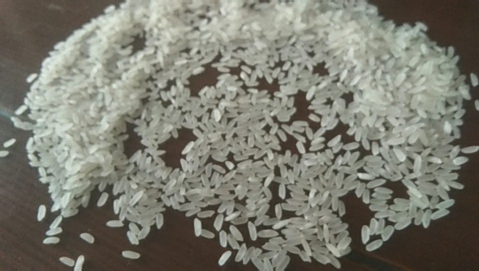 厨房场景照片:一位家庭主妇正在将刚煮好的长粒香米饭盛入白瓷碗中,蒸汽袅袅上升,米粒颗颗分明、晶莹剔透,旁边摆放着开盖的大米包装袋,清晰可见‘长粒香大米’字样和产地信息 家庭烹饪长粒香米饭场景图