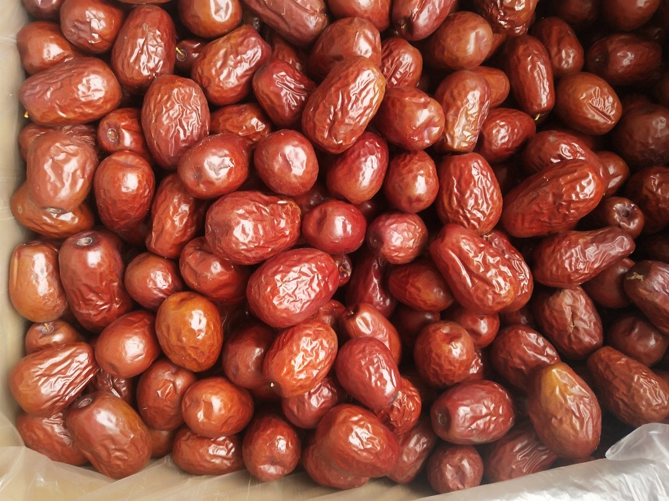 孕妇正在食用干红枣片,背景为厨房环境,桌上摆放着红枣干、水果和坚果 孕妇食用干红枣片