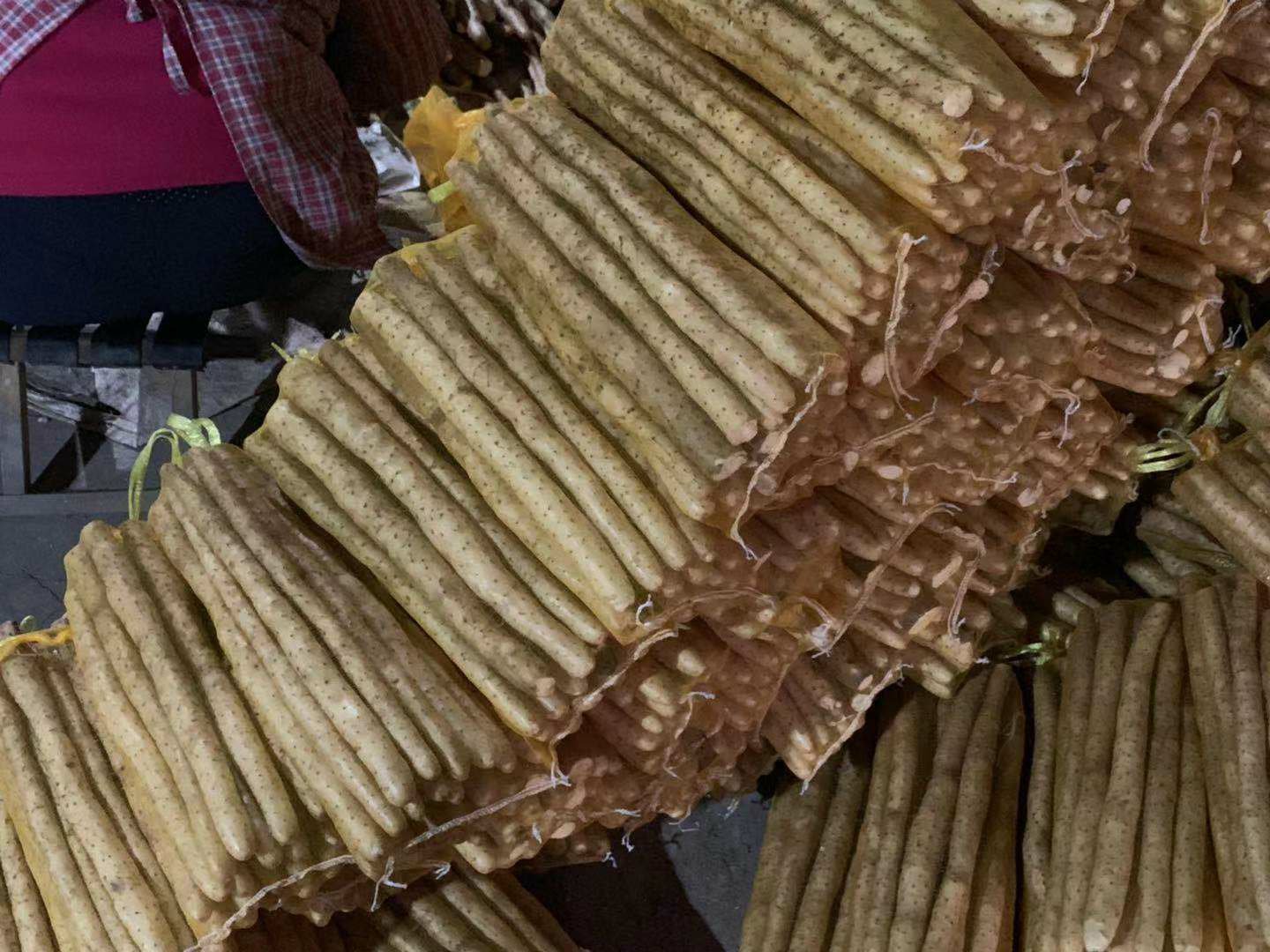 超市蔬菜区一排整齐摆放的带泥新鲜山药,部分已被挑选留下空位,一只女性的手正在拿起一根山药检查,背景虚化体现真实购物环境,光线明亮清晰 超市货架上整齐陈列的新鲜山药与正在挑选的顾客手部特写