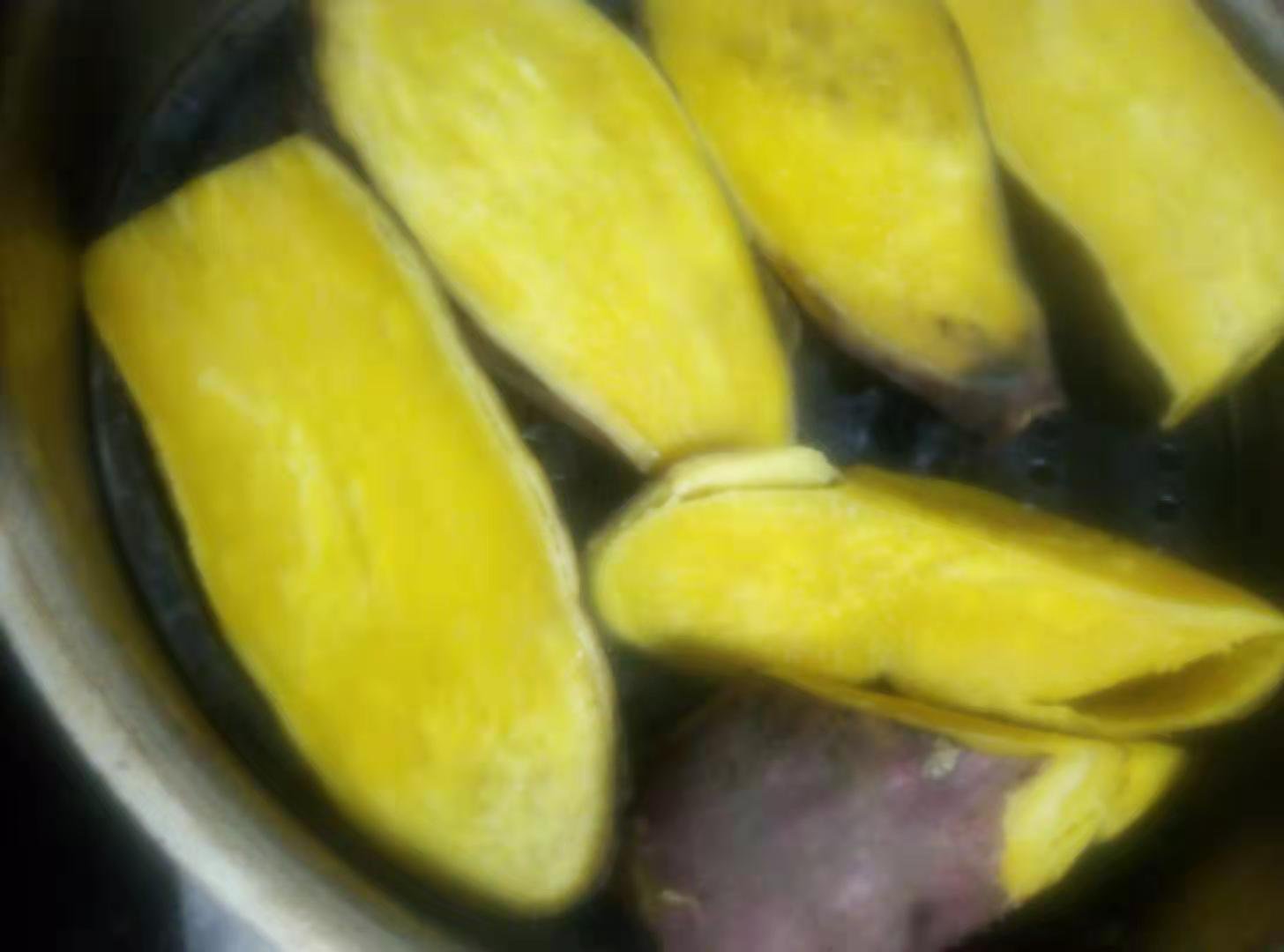 一根已经蒸熟并剥去外皮的商薯19,横向剖开显示内部金黄色的薯肉,质地细腻无明显纤维条纹,表面轻微起沙,散发热气,背景为木质砧板和竹筷,体现家庭餐桌场景 蒸熟后的商薯19剖面展示其细腻金黄的薯肉质地