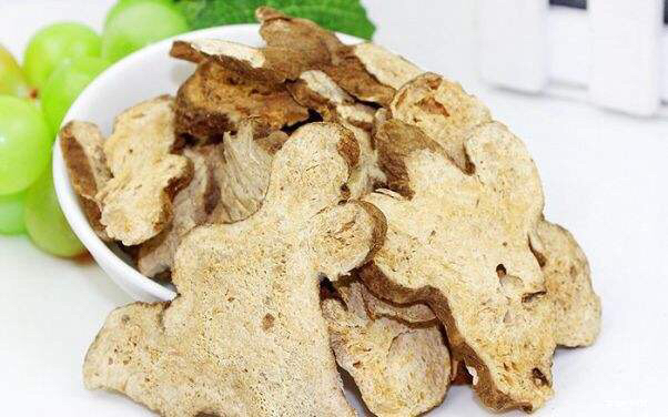 一位中年女性正在家中服用白术片,桌上摆放有温水和药盒,背景为温馨的家庭环境 白术片使用场景图