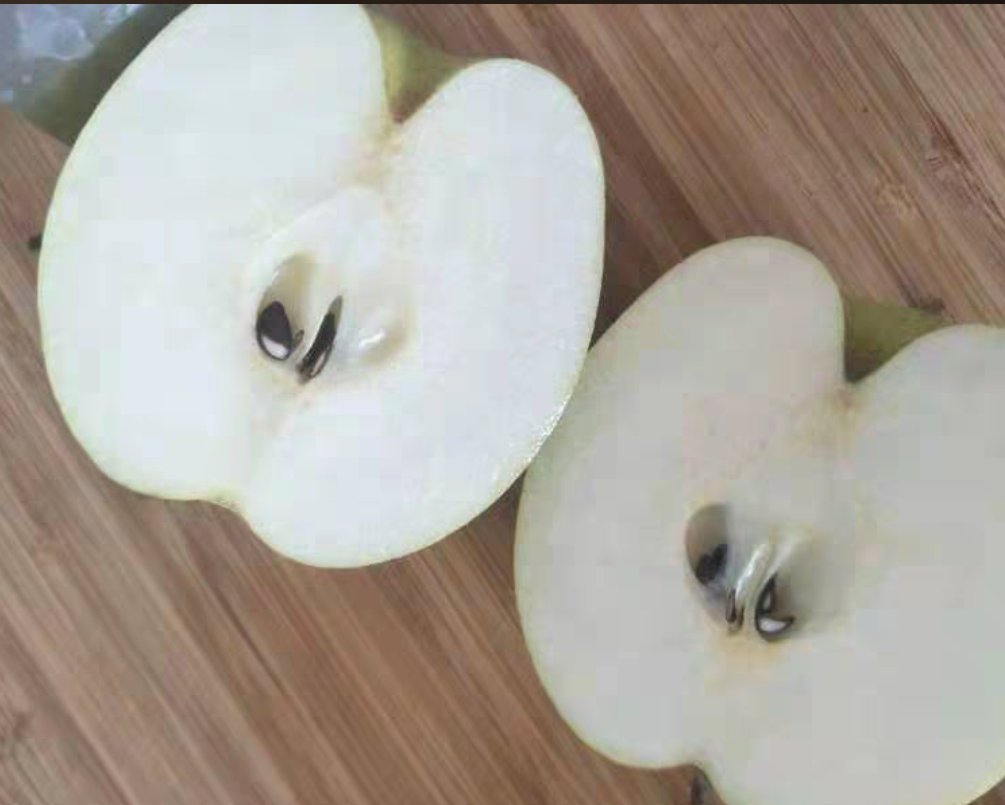 新鲜雪梨被纵向剖成两半,果核清晰可见,使用金属小勺正在剔除深色梨籽,背景为木质砧板 雪梨对半切开后露出梨核,一只手持小勺正在挖除黑色梨籽