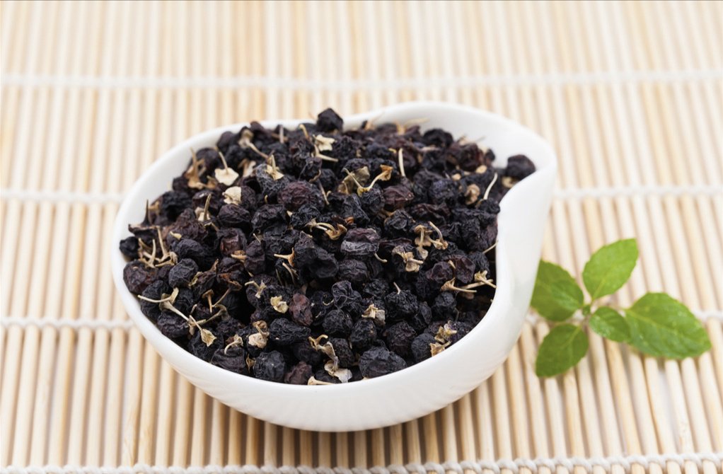 一张俯拍图展示黑枸杞的多种食用方式:左侧为黑枸杞与菊花、麦冬混合泡茶;中部为加入燕麦粥的早餐碗;右侧为制成冻干粉用于温水冲服,背景为简约木质餐桌,体现日常养生场景 黑枸杞食疗搭配示意图