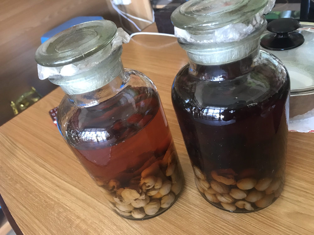 透明玻璃泡酒罐内可见深琥珀色酒液,沉浮着膨胀的桂圆肉块和未溶解的冰糖颗粒,罐身无水渍,标签标注‘桂圆酒-2024.09.01’,背景为木质储物架,光线柔和 玻璃泡酒罐中浸泡中的桂圆酒特写
