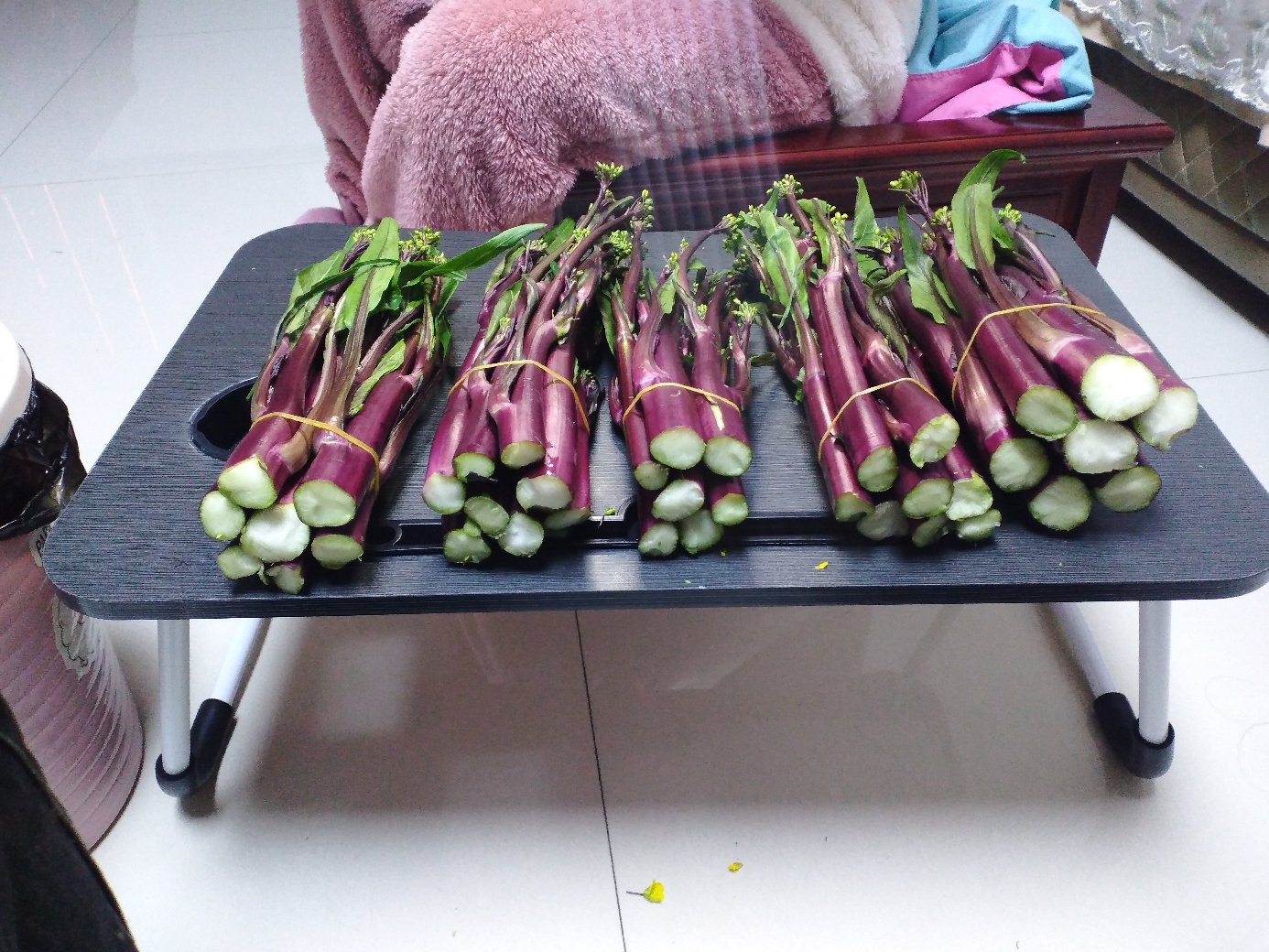 一名厨师正在厨房操作台上清洗一把新鲜的红菜苔,旁边有削皮刀、砧板和切好的红菜苔段,茎呈紫红色,叶片翠绿,背景整洁明亮 红菜苔的清洗与切段处理过程