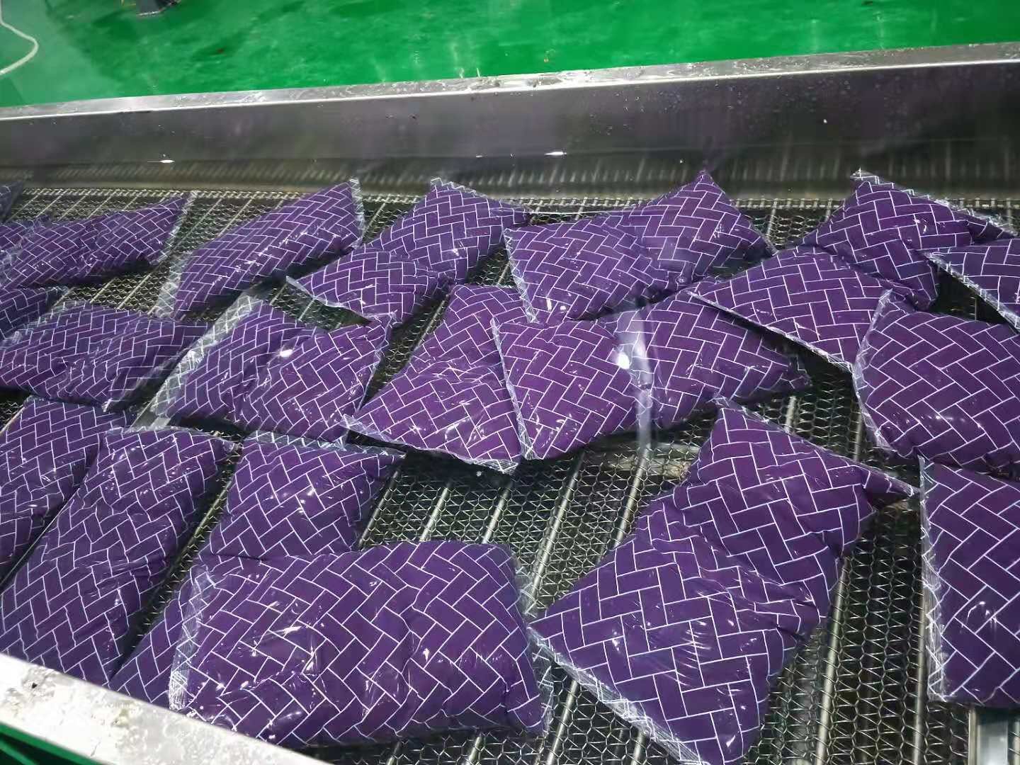 工厂流水线上,紫薯泥正在通过金属模具被挤压成细长的米状条带,设备周围有蒸汽升腾,操作工人身穿防护服监控参数,背景可见传送带将成型后的湿米送往下一工序 紫薯米生产线中的挤压成型环节