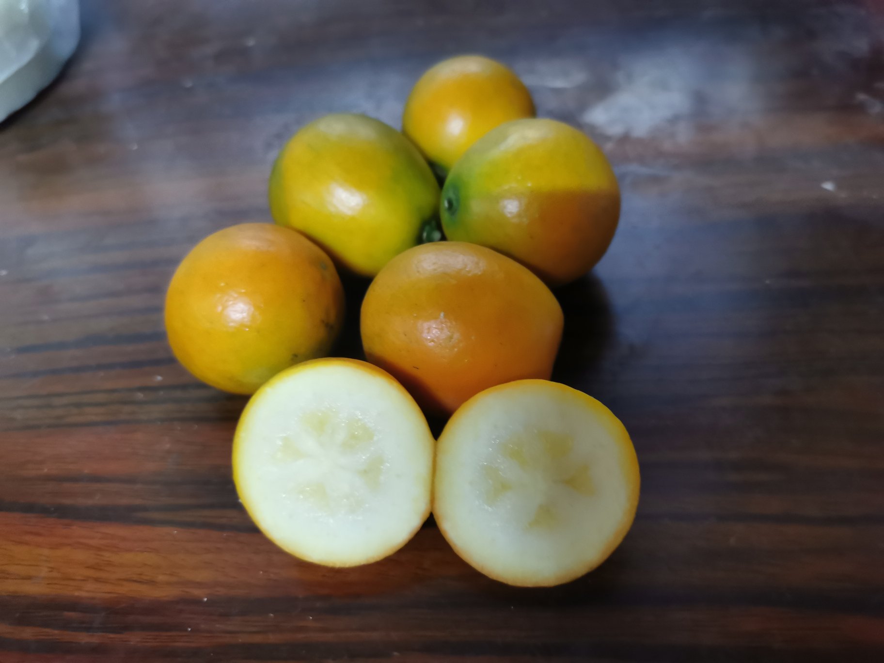 一杯透明玻璃杯中盛放着几颗金桔片泡在水中,旁边放着新鲜的金桔果实,背景为木质桌面 金桔泡水喝有什么功效