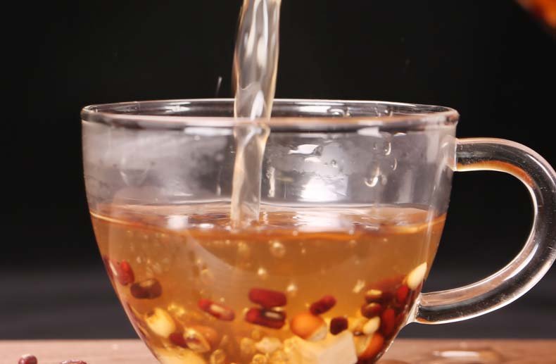 一位中年女性在厨房用玻璃壶煮黑豆水的场景