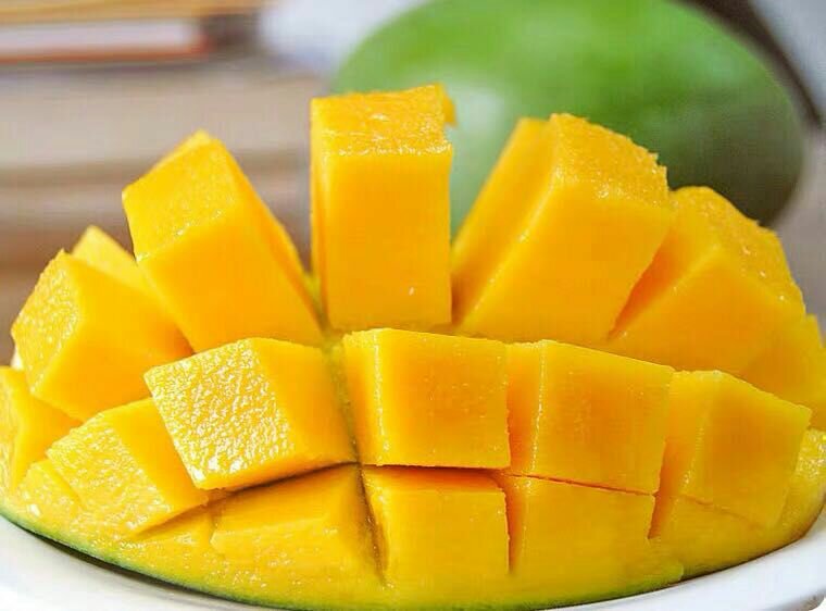 近距离拍摄的切开大青芒,展示其厚实的金黄色果肉、半透明质感及紧贴果肉的扁平果核,果肉边缘带有微微的纤维纹理,背景为白色瓷盘,突出食物美感 切开的大青芒特写图