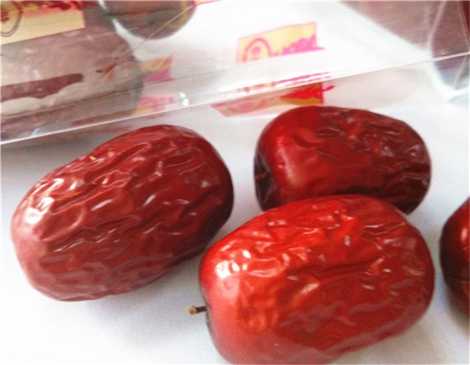 新疆若羌产区新鲜采摘的长枣,呈深红色,果形细长饱满,表面有天然光泽,背景为戈壁绿洲中的枣园,阳光充足,土壤呈沙质 若羌长枣特写