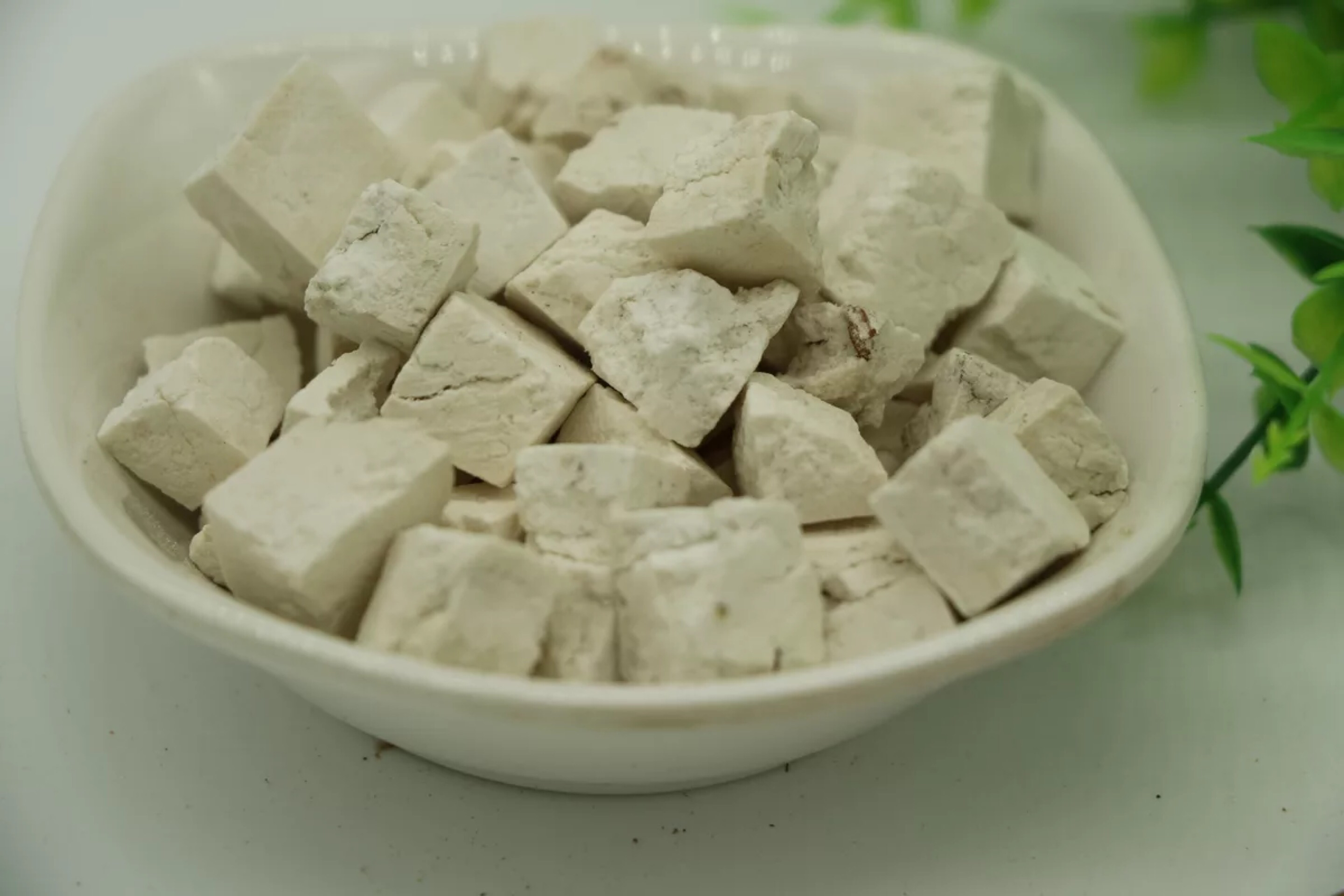 中医师正在配伍熟地黄与茯苓、白术饮片：木质药斗柜前，手执不锈钢药匙，将棕黑色熟地黄片与米白色茯苓块、灰白色白术片按6:3:3比例分装入青花瓷药碗