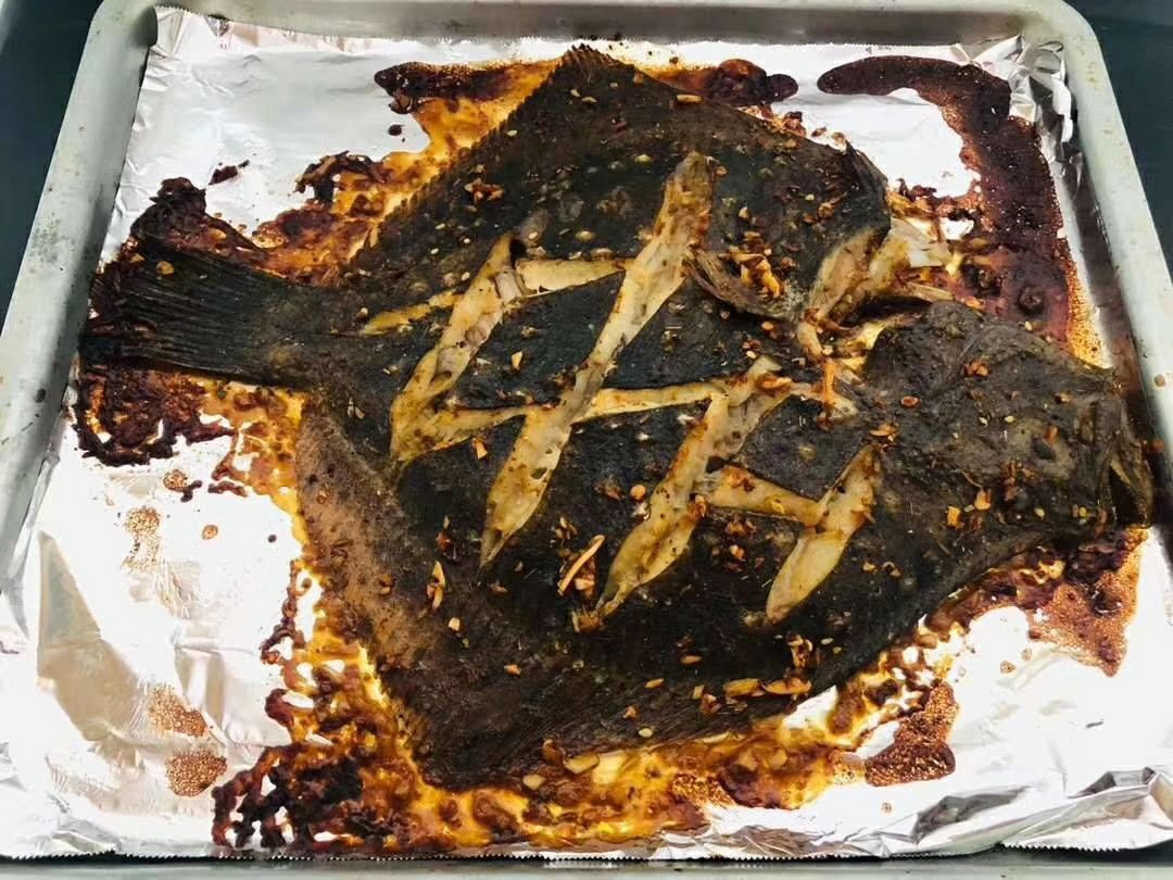 一条多宝鱼正放在烤箱内的金属烤架上,表面呈现金黄色,微微焦化,周围有蒸汽上升,烤箱灯光照亮食物,背景虚化,突出烤制过程的诱人感 烤箱中正在烘烤的多宝鱼