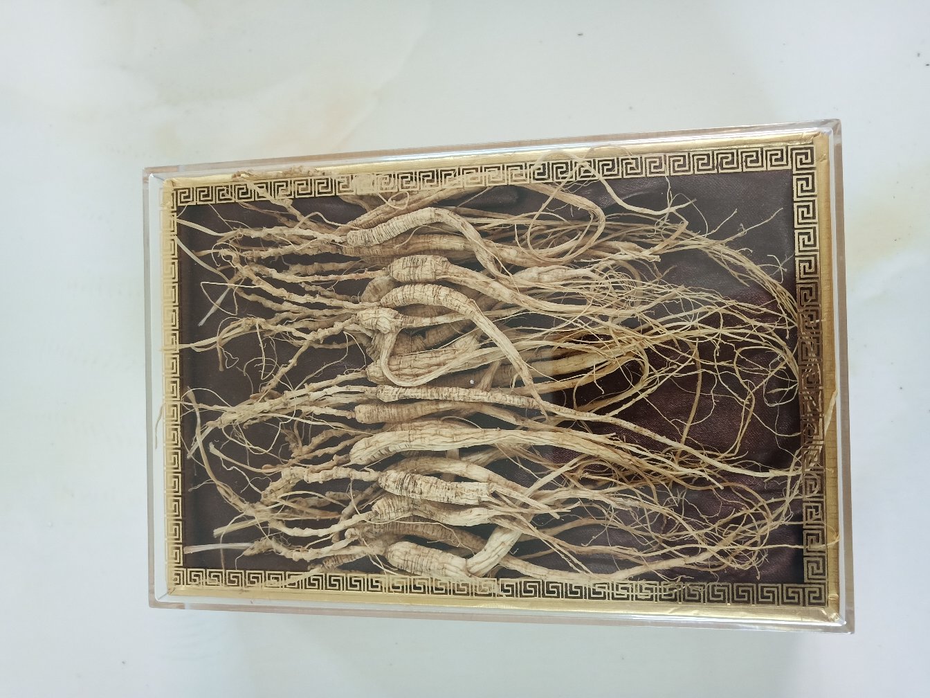 一组精心整理的野山参干品陈列于木质托盘上,参体呈纺锤形或人形,表面棕黄色带有清晰铁线纹,芦碗层层叠叠,须根细长如虾须并附着珍珠点,旁边配有放大镜和测量尺,用于展示细节特征,背景为中国传统红木柜与书法‘参王’字样,凸显高端礼品属性 柳河云岭野山参成品展示