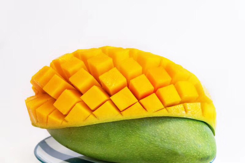 一颗被横向剖开的大青芒,露出金黄细腻的果肉,汁水微微渗出,刀口光滑无纤维感,旁边摆放着小勺和果盘,展示其极佳的食用品质 切开的攀枝花大青芒特写