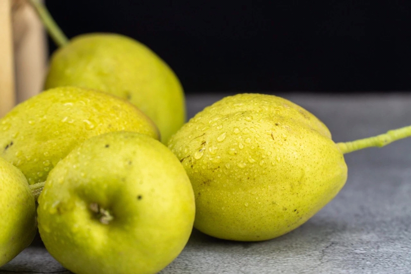 高清近距离拍摄的酸巴梨果实,展示其黄绿带红晕的果皮、明显的果点和凹陷的果蒂,切开后果肉呈乳白色,质地紧实,可见细微纤维结构,背景虚化突出主体 酸巴梨果实特写