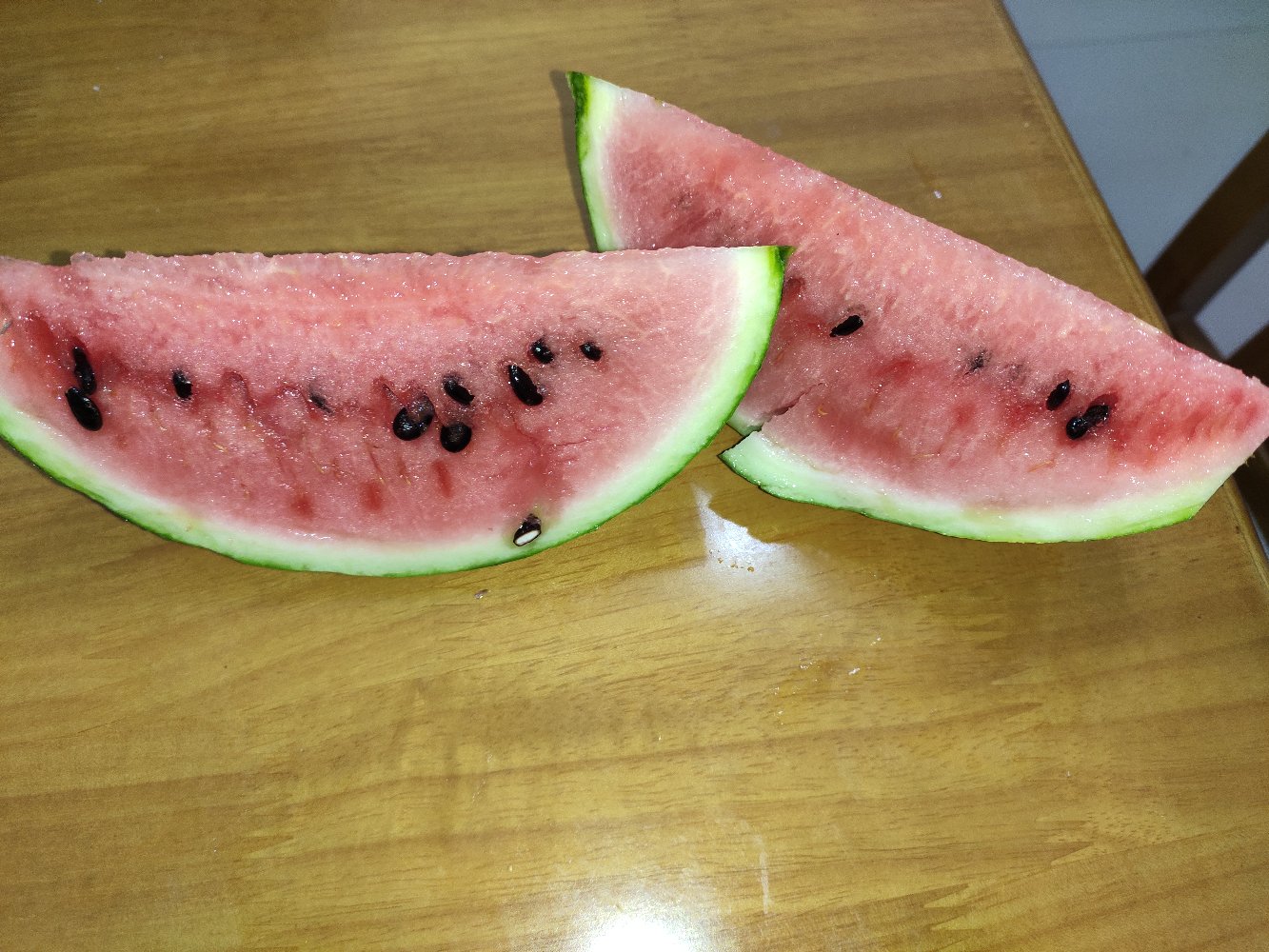 一颗被切开的京欣西瓜,露出鲜艳红润的果肉,水珠清晰可见,背景为木质桌面,营造自然清新的氛围 京欣西瓜切开图