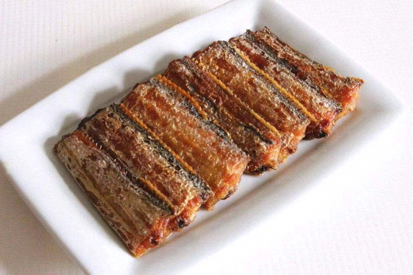 一盘刚出锅的煎带鱼摆放在白色瓷盘中,鱼身两面金黄酥脆,边缘微焦,表面略带油光,旁边点缀香菜和柠檬片,背景虚化,突出食物色泽诱人 煎带鱼成品特写