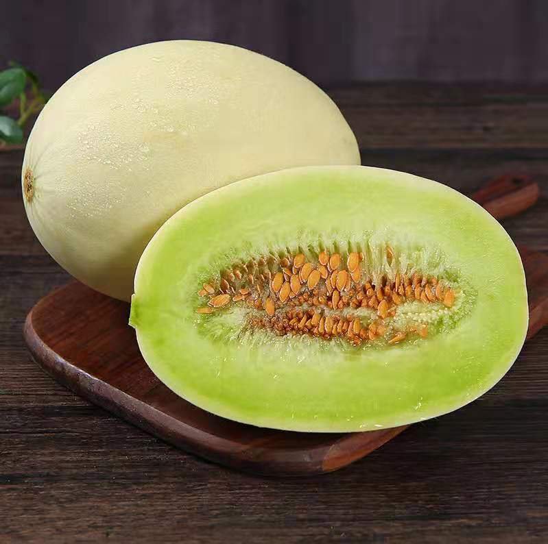 展示一颗完整的玉菇甜瓜,果皮洁白光滑,果肉呈淡绿色,切开后可见内部籽粒清晰,背景为自然田园环境 玉菇甜瓜特写