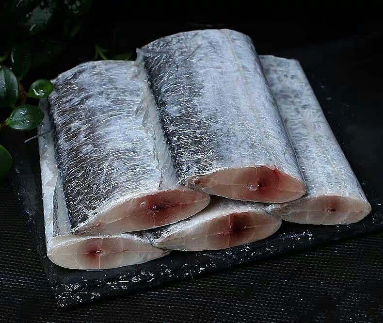 一条新鲜带鱼被横向剖开,清晰可见其腹腔内附着的一层灰白色至淡黄色颗粒状物质,即为带鱼籽;周围有少量透明黏液和血丝,背景为白色砧板,旁边放有厨房剪刀和刷子 带鱼腹部剖开显示内部灰白色鱼籽