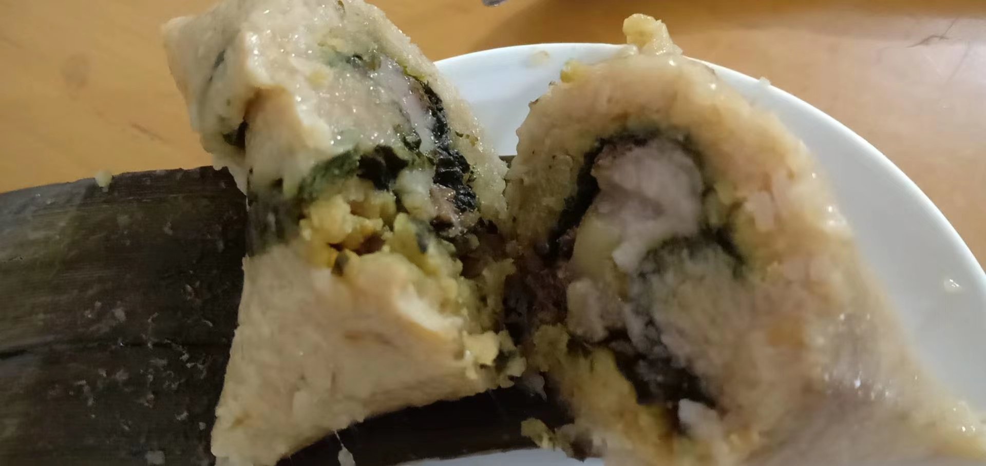 高清微距摄影:剖开一只刚出锅的羊肚菌鲜肉粽,可见琥珀色糯米晶莹半透明,嵌有3–5粒深褐色羊肚菌子囊果断面,菌褶清晰可见;粽叶脉络完整,无碱斑;背景虚化呈现蒸汽氤氲效果 羊肚菌粽子实物切面特写