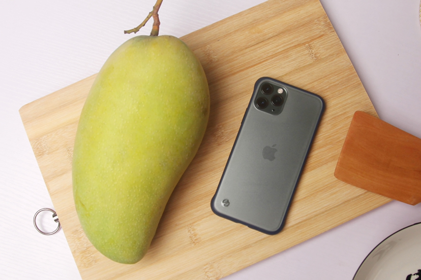 芒果果实与种子关联展示:强调品种典型性与种子解剖结构,背景为原木色砧板,自然侧光突出纹理细节 成熟芒果果实与新鲜果核并置图:左侧为金黄色带红晕的成熟芒果(表皮光滑泛蜡质光泽),右侧为刚剥离的棕褐色椭圆形芒果核(表面覆盖浅棕色纤维层,一端可见明显种脐凹陷)