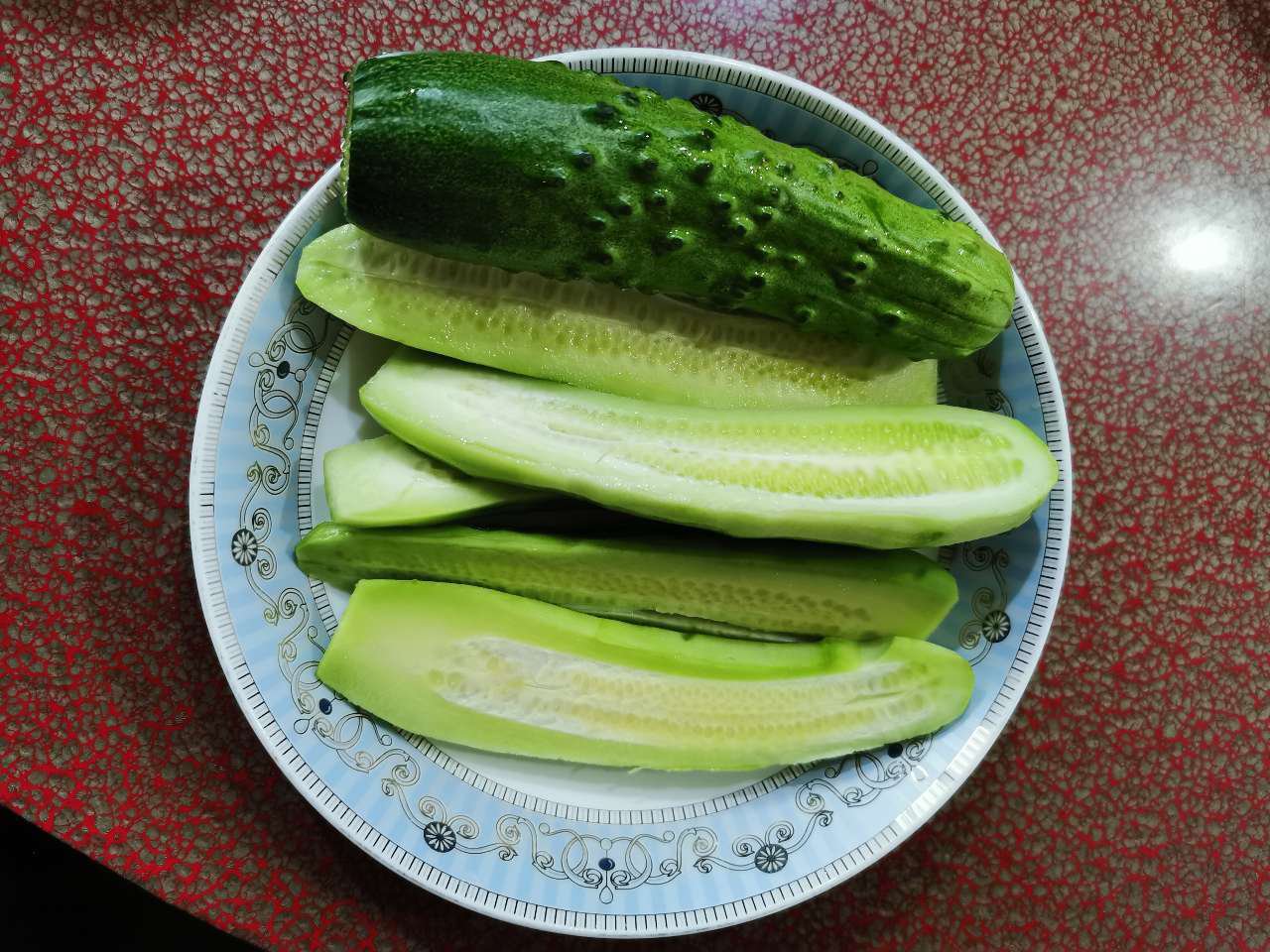 白色瓷盘中摆放着一根被横向切开的旱黄瓜,露出浅绿色致密果肉与较小的籽腔,断面湿润有光泽,旁边配有不锈钢刀具和柠檬片,展现食材新鲜度 厨房中切开的旱黄瓜横切面特写