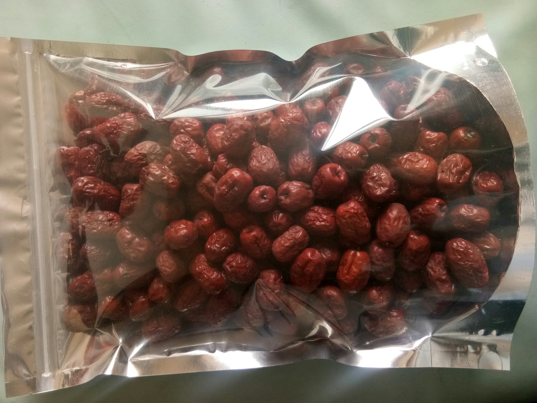 金丝小枣粒成品高清特写,展现标准颗粒尺寸、透亮色泽与干燥度,体现工业化分级包装品质 金丝小枣粒成品特写:颗粒均匀饱满,表面微泛琥珀光泽,大小约6×4mm,散铺于食品级白瓷盘中,背景虚化呈现现代化洁净车间流水线