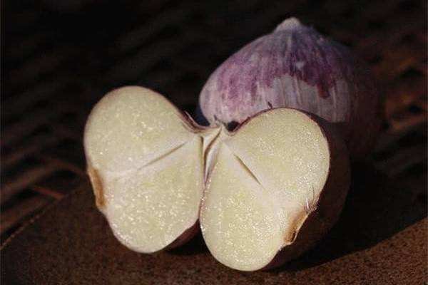 左侧为切开的独头蒜,内部为单一完整蒜瓣,质地致密金黄;右侧为普通多瓣大蒜的一个蒜瓣,两者大小相近,用于展示组织结构差异 独头蒜切面与普通大蒜对比图