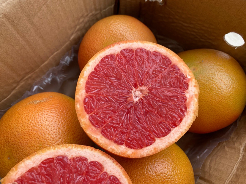 一个新鲜的葡萄柚被切开,露出粉红色果肉,背景为木质桌面 葡萄柚果实特写