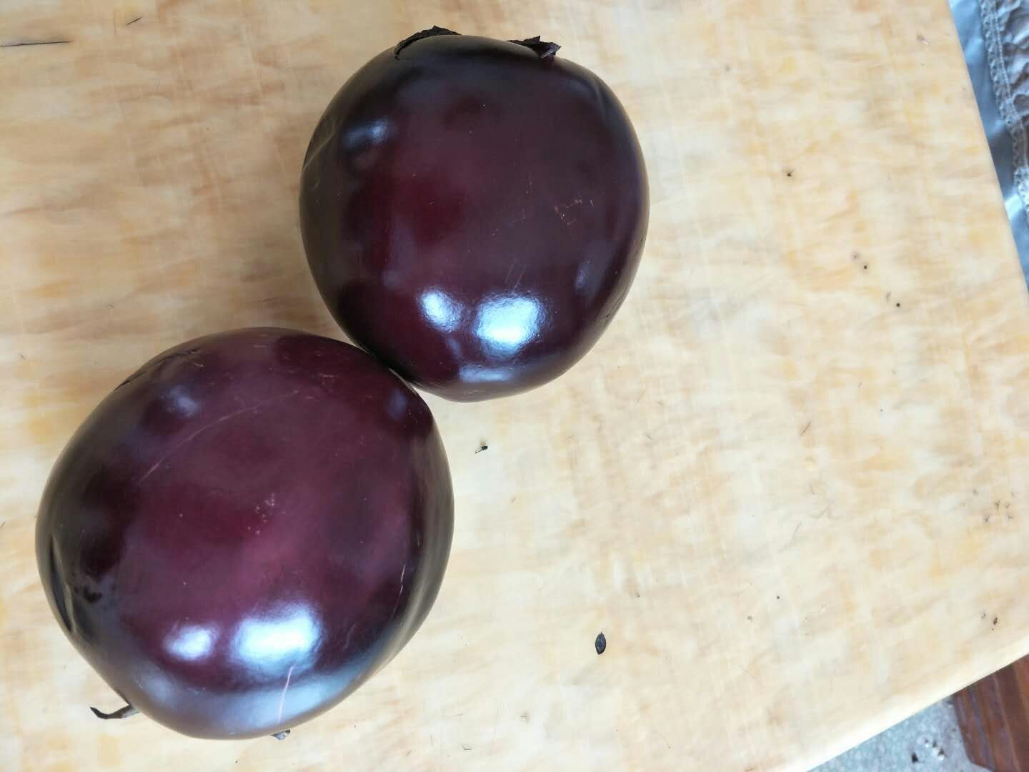 左侧为一串成熟的蓝靛果,深蓝色浆果成对生长于细枝上,表面有明显白霜;右侧为一根紫黑色长条茄子,表皮光滑油亮,置于木质砧板上,背景为自然光下的厨房环境 成熟蓝靛果与普通茄子对比图