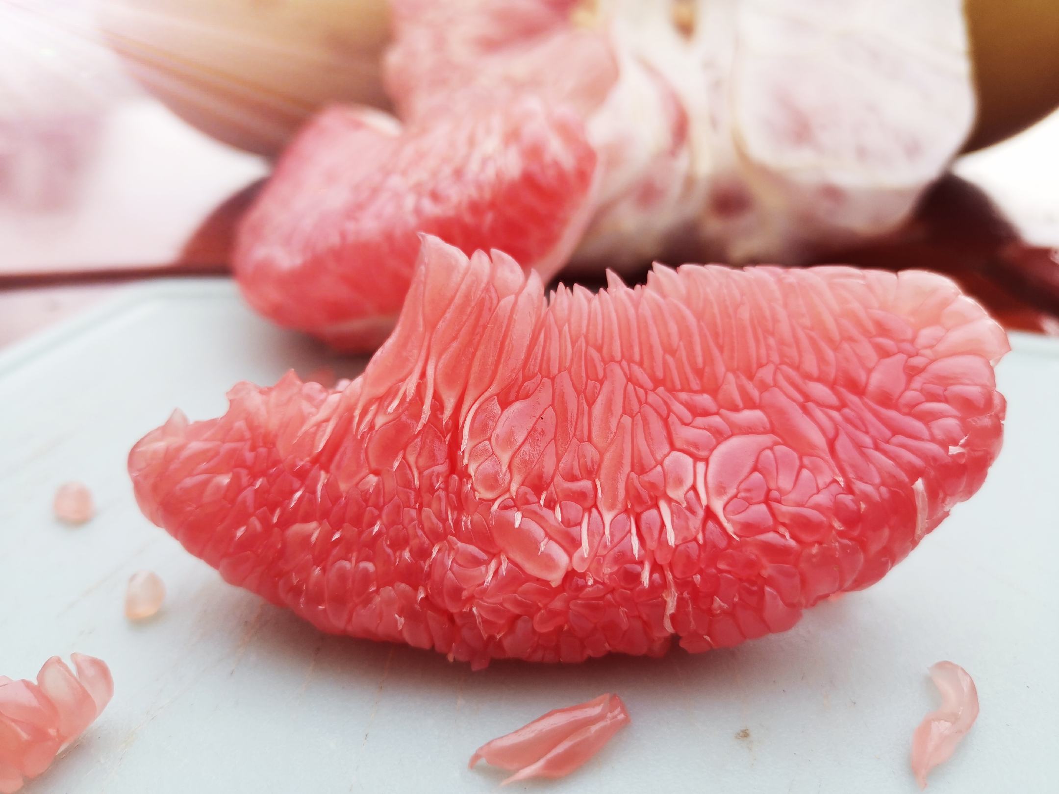 三红蜜柚果肉与果汁特写：半透明粉红果瓣整齐排列，果汁滴落瞬间呈现高黏度拉丝状态，背景散落新鲜柚皮碎屑