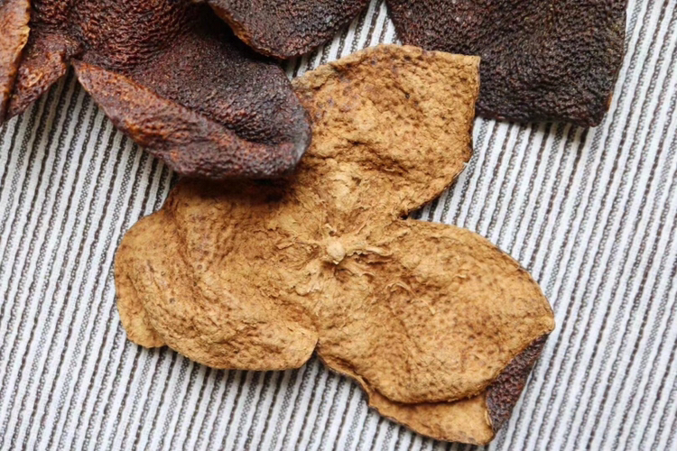 左侧为不同年份的茶枝柑陈皮干片,按三年、五年、八年、十年顺序排列,颜色由棕红渐变为黑褐,表面褶皱加深;右侧为实际应用场景:一碗广式老火靓汤旁放有掰碎的陈皮,一杯透明玻璃壶中漂浮着陈皮与茶叶,还有一本打开的笔记本记录‘2020年收藏500g圈枝梅江陈皮’字样,背景虚化处可见木质货架陈列多罐密封陈皮 茶枝柑陈皮成品展示与应用场景组合图