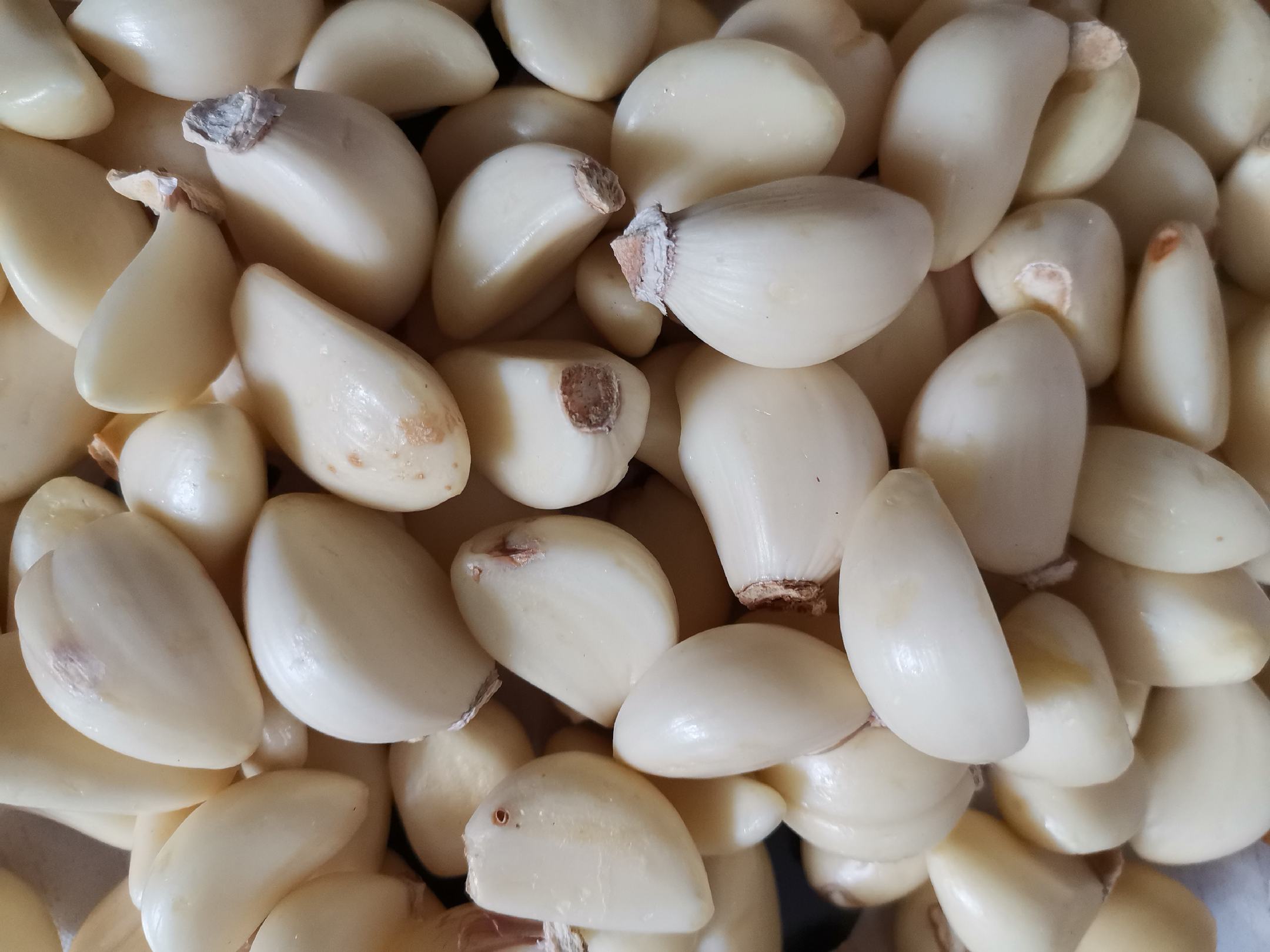 手持木质蒜杵在石臼中研磨白色蒜米的特写镜头，背景虚化的厨房台面上散落几瓣去皮新鲜大蒜，光线柔和温暖，突出手工制作的质感