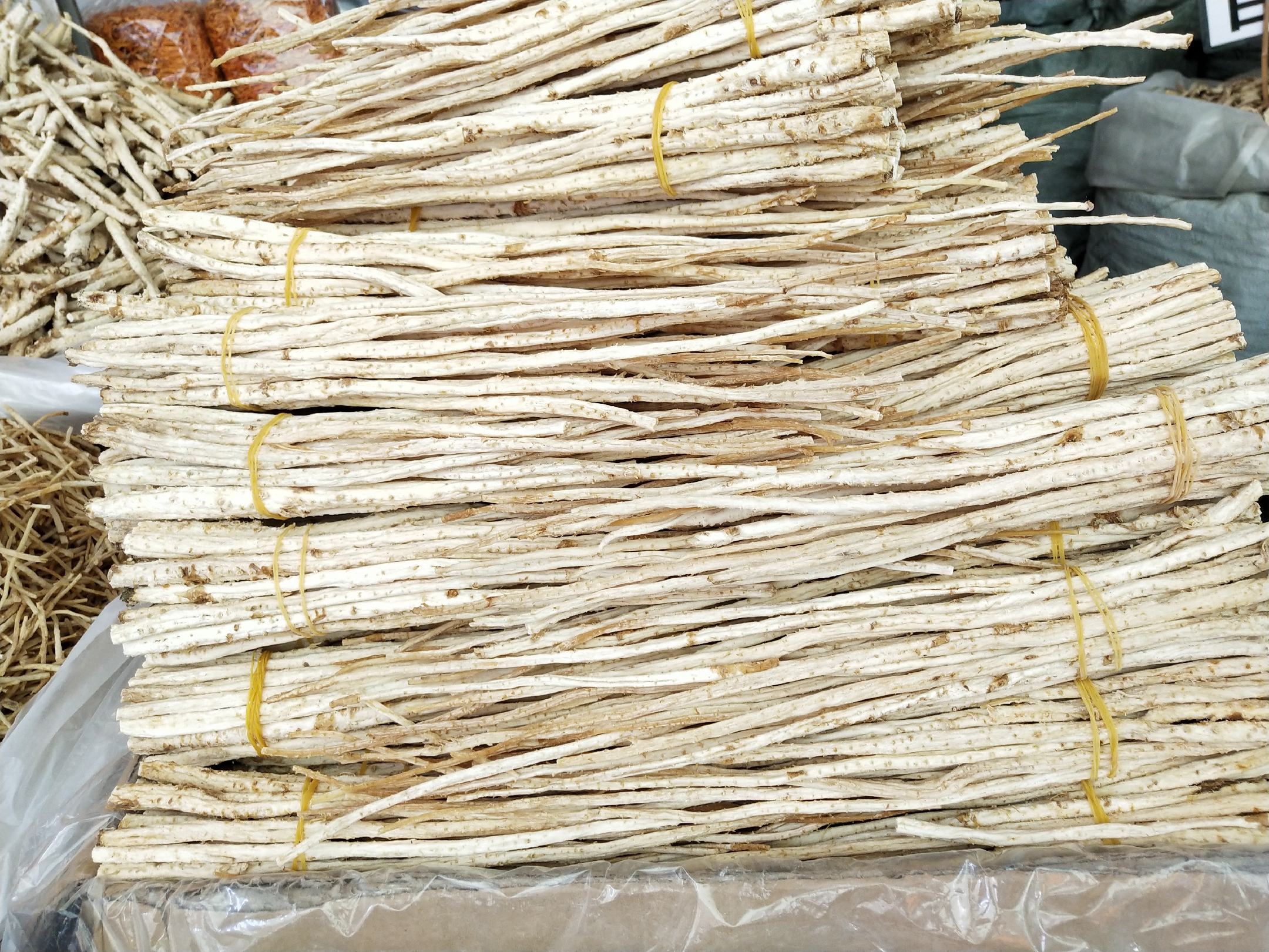 一捆干燥的北沙参药材,呈细长圆柱形,颜色为淡黄白色,表面有明显的纵向纹理和细小根痕,整齐捆扎成把,背景为木质中药柜,体现传统药材交易场景 北沙参原药材特写